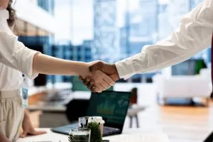 Corporate professionals shaking hands over a desk in a modern office, representing a successful leadership transition and executive recruitment placement for an agribusiness.