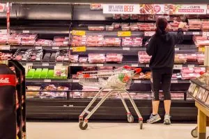 A consumer selects fresh Australian beef from a supermarket retail shelf, illustrating the end of the FMCG commercial food supply chain.
